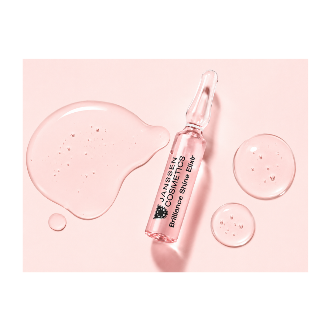 Janssens Cosmetics Brilliance Shine Elixir bottle on a pink background with droplets.